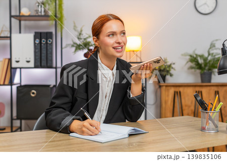 Young businesswoman talking on smartphone call with client writing notes seals big business deal Young businesswoman talking on smartphone call with client writing notes seals big business deal 139835106
