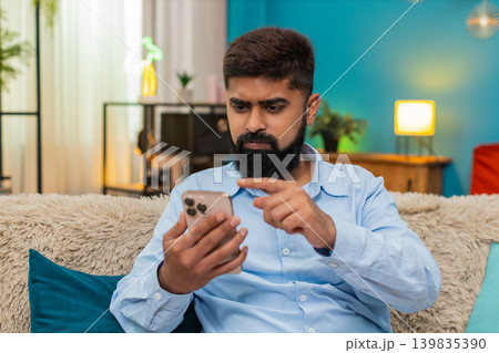 Indian man frowns at bad smartphone message shakes head closes chat app showing frustration indoors Indian man frowns at bad smartphone message shakes head closes chat app showing frustration indoors 139835390