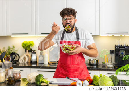 Arabian young adult man eating fresh salad in kitchen enjoying keto diet healthy nutrition lifestyle Arabian young adult man eating fresh salad in kitchen enjoying keto diet healthy nutrition lifestyle 139835438