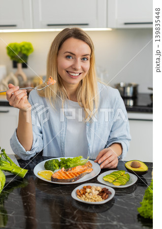 Young woman eating keto lunch with trout avocado nuts and fresh vegetables for healthy weight loss 139835448