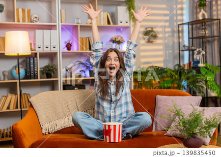 Young woman on home sofa eating popcorn and cheering favorite team during exciting live sports match Young woman on home sofa eating popcorn and cheering favorite team during exciting live sports match 139835450