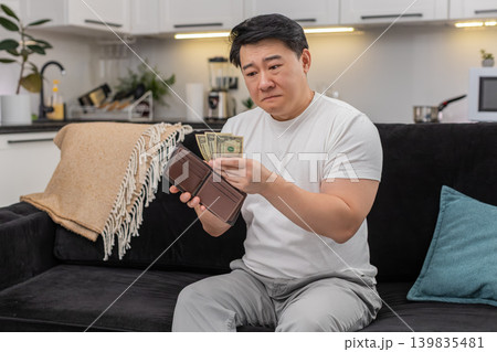 Asian man checks wallet sees only small dollar bills frowns and sets saving goal for budget plan new 139835481