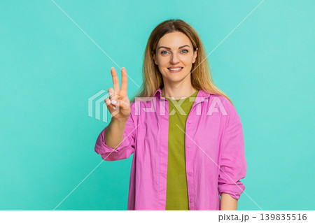 Woman showing peace sign with two fingers and smiling expressing positivity harmony and friendliness Woman showing peace sign with two fingers and smiling expressing positivity harmony and friendliness 139835516