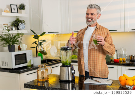 Middle-aged man making green smoothie with blender in kitchen at home for healthy fitness diet plan Middle-aged man making green smoothie with blender in kitchen at home for healthy fitness diet plan 139835529