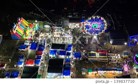 An aerial top-down view of a vibrant night market and amusement park illuminated by colorful neon lights. An aerial top-down view of a vibrant night market and amusement park illuminated by colorful neon lights. 139837710