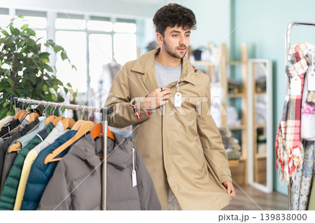 Guy try on raincoat in front of mirror in clothes store Guy try on raincoat in front of mirror in clothes store 139838000