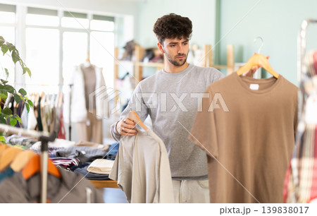 Bearded young man choosing t-shirts in fashion boutique 139838017