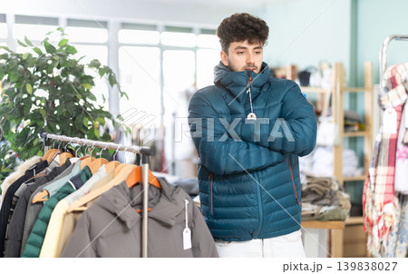 Young man trying on down jacket in store Young man trying on down jacket in store 139838027
