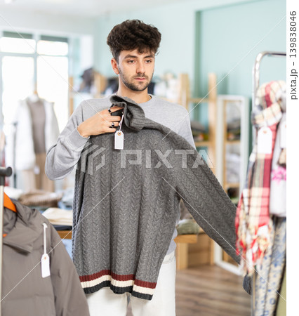 Young man chooses sweater in clothing store Young man chooses sweater in clothing store 139838046
