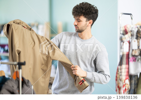 Young man choosing raincoat in clothing store Young man choosing raincoat in clothing store 139838136