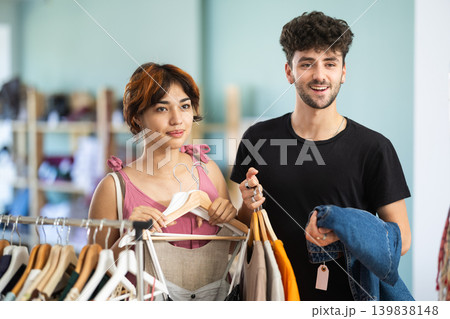 Young couple chooses fashionable dresses and t-shirt in clothing store Young couple chooses fashionable dresses and t-shirt in clothing store 139838148