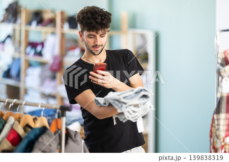 While shopping, guy scans barcode on label of jeans 139838319