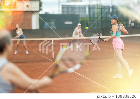 Young and elderly women playing doubles tennis Young and elderly women playing doubles tennis 139838320