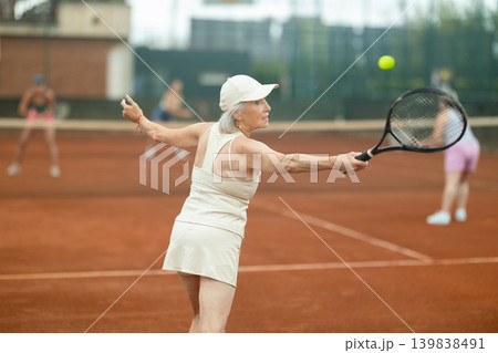 Aged woman enthusiastically playing tennis outdoors in summer 139838491