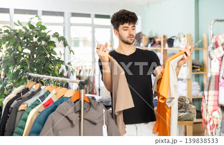 Young man chooses t-shirt in clothing store Young man chooses t-shirt in clothing store 139838533