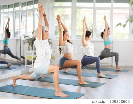 Woman performing revolved side angle pose Parivrtta Parsvakonasana during yoga class with female group in fitness studio Woman performing revolved side angle pose Parivrtta Parsvakonasana during yoga class with female group in fitness studio 139838600