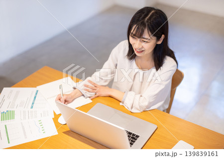 デスクに資料を広げパソコン作業しながらメモを取る日本人の若い女性 139839161
