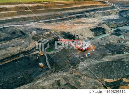Massive dragline excavator at work in a sprawling open-pit coal mine. Several haul trucks transport excavated material Massive dragline excavator at work in a sprawling open-pit coal mine. Several haul trucks transport excavated material 139839511