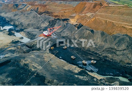 Massive dragline excavator at work in a sprawling open-pit coal mine. Several haul trucks transport excavated material 139839520
