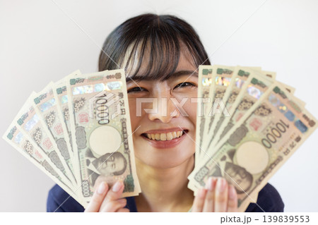 10枚の1万円札を広げて持ち、微笑む日本人の若い女性 139839553