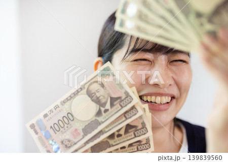 10枚の1万円札を広げて持ち、微笑む日本人の若い女性 139839560