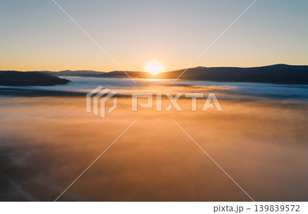 Warm sunlight illuminates a thick layer of golden fog blanketing a wide valley at sunrise 139839572