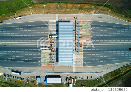 A wide aerial view shows a modern toll plaza with multiple lanes on a highway. A wide aerial view shows a modern toll plaza with multiple lanes on a highway. 139839622