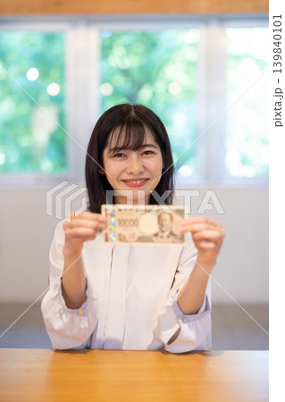 1万円札を手に微笑む日本人の若い女性 139840101