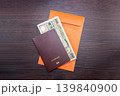 International passport and banknote placed on an orange envelope and a brown dark wood background. Top view. 139840900