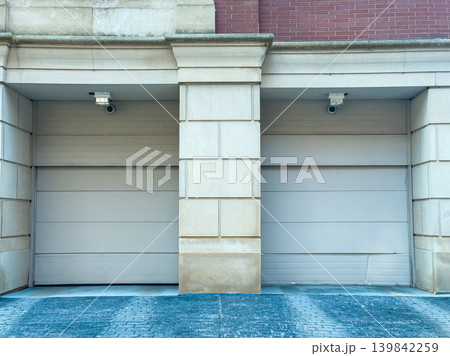 Two garage doors with security cameras installed on the walls, located in an urban area, taken during daylight hours Two garage doors with security cameras installed on the walls, located in an urban area, taken during daylight hours 139842259