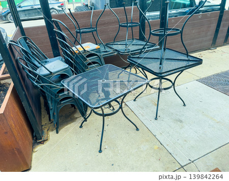 Chairs and tables stacked outside a cafe on a city street during the afternoon hours 139842264
