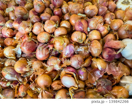Fresh shallots are stacked in a market setting during the daytime, showcasing their unique shapes and colors 139842266