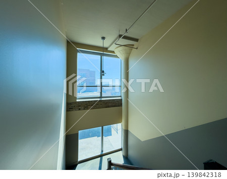 Light enters through a large window in a quiet stairwell during the day in a modern building 139842318