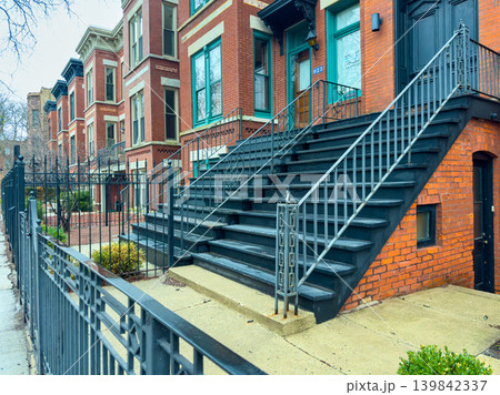 Steps lead to brick building in a city neighborhood with fences and plants around during a cloudy day 139842337