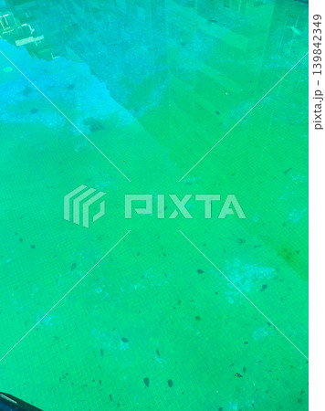 Water in a pool shows green color with dirt and debris floating on surface, capturing urban environment below on a sunny day Water in a pool shows green color with dirt and debris floating on surface, capturing urban environment below on a sunny day 139842349