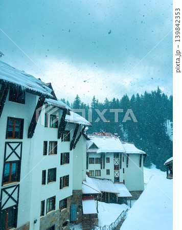 Snow falls on buildings in a mountain village during winter in a forested area in a remote location Snow falls on buildings in a mountain village during winter in a forested area in a remote location 139842353