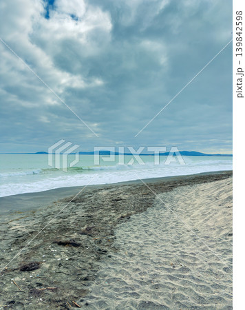 Cloudy day at the beach with waves and distant mountains in the background near the shore Cloudy day at the beach with waves and distant mountains in the background near the shore 139842598