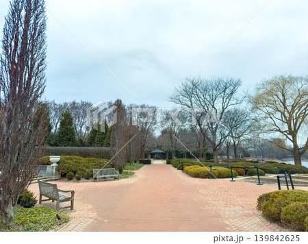 Path through a park with benches and trees during a cloudy day in early spring near the water in a city setting 139842625
