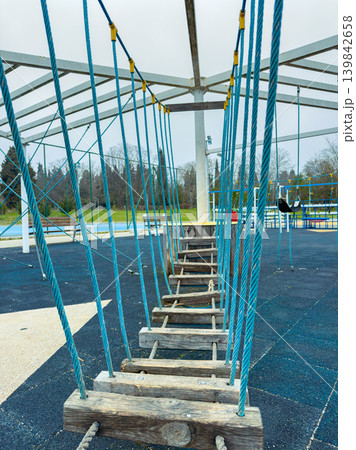 Swing bridge connects two platforms in a playground during a cloudy day with trees in the background Swing bridge connects two platforms in a playground during a cloudy day with trees in the background 139842658
