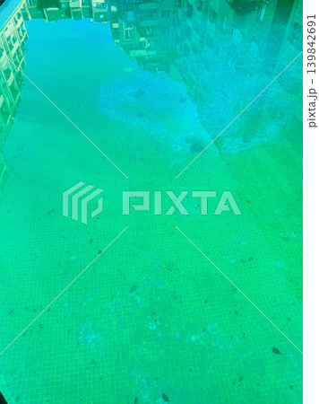Clear water in a pool reflects buildings nearby during daytime showing a bright green color with some fish swimming under the surface Clear water in a pool reflects buildings nearby during daytime showing a bright green color with some fish swimming under the surface 139842691