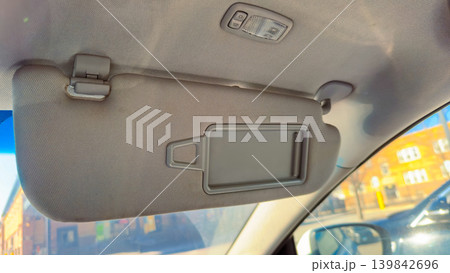 Car sun visor with a mirror set inside a vehicle showing part of the interior during daylight on a sunny day 139842696