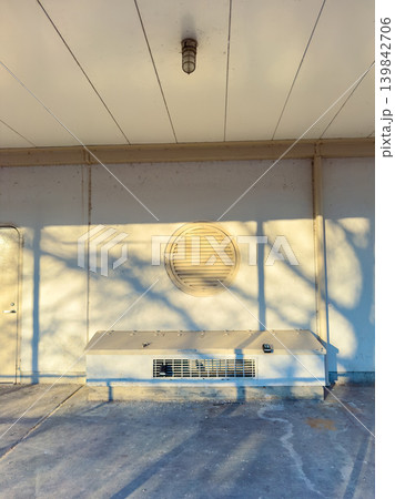 Sunlight casts shadows on a building wall with a circular vent and an air conditioning unit during the late afternoon Sunlight casts shadows on a building wall with a circular vent and an air conditioning unit during the late afternoon 139842706