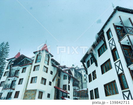 Snow falls on mountain resort buildings in a winter landscape during a cold day in a snowy location 139842711