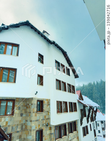 Snow falls gently on a mountain lodge surrounded by trees during winter in a remote area, capturing a scenic view of the building and snowy landscape 139842716