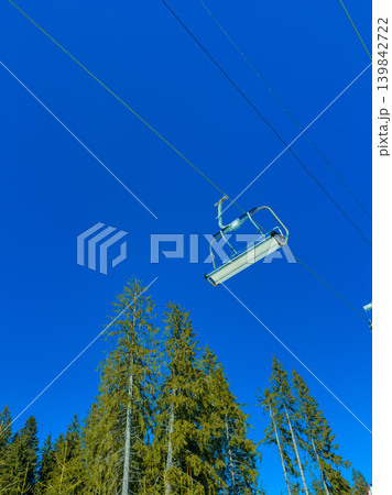 Ski lift moves up the mountain under clear blue sky in winter landscape surrounded by tall trees Ski lift moves up the mountain under clear blue sky in winter landscape surrounded by tall trees 139842722