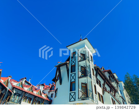 Building with a tower on a clear day in a mountain area with blue skies and nearby trees, showing a blend of architecture and nature 139842729
