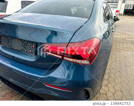 Blue car parked on wet pavement in auto lot during a cloudy day with water droplets on the surface Blue car parked on wet pavement in auto lot during a cloudy day with water droplets on the surface 139842752