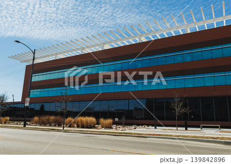 Modern building with glass facade located along a city street on a clear day with blue sky and clouds during afternoon 139842896