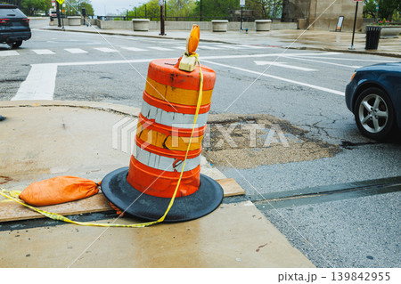 Traffic cone placed near a street to indicate construction activity on a rainy day in an urban area Traffic cone placed near a street to indicate construction activity on a rainy day in an urban area 139842955