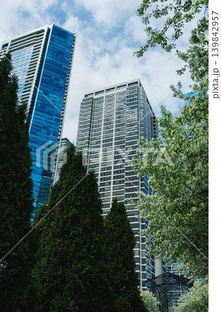 Tall buildings stand alongside trees in a city setting during a cloudy day with hints of blue in the sky Tall buildings stand alongside trees in a city setting during a cloudy day with hints of blue in the sky 139842957